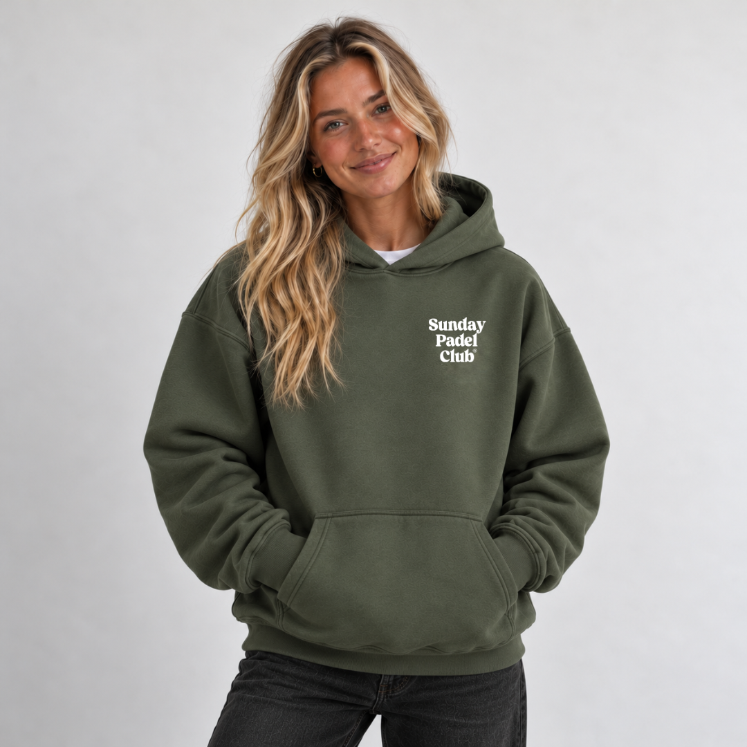 PSF Collective A smiling woman with long blonde hair wears an olive green Sunday Padel Club Hoodie in Cypress featuring white text on the left chest, a large front kangaroo pocket, and a plain light gray background. Designed for the Unwind