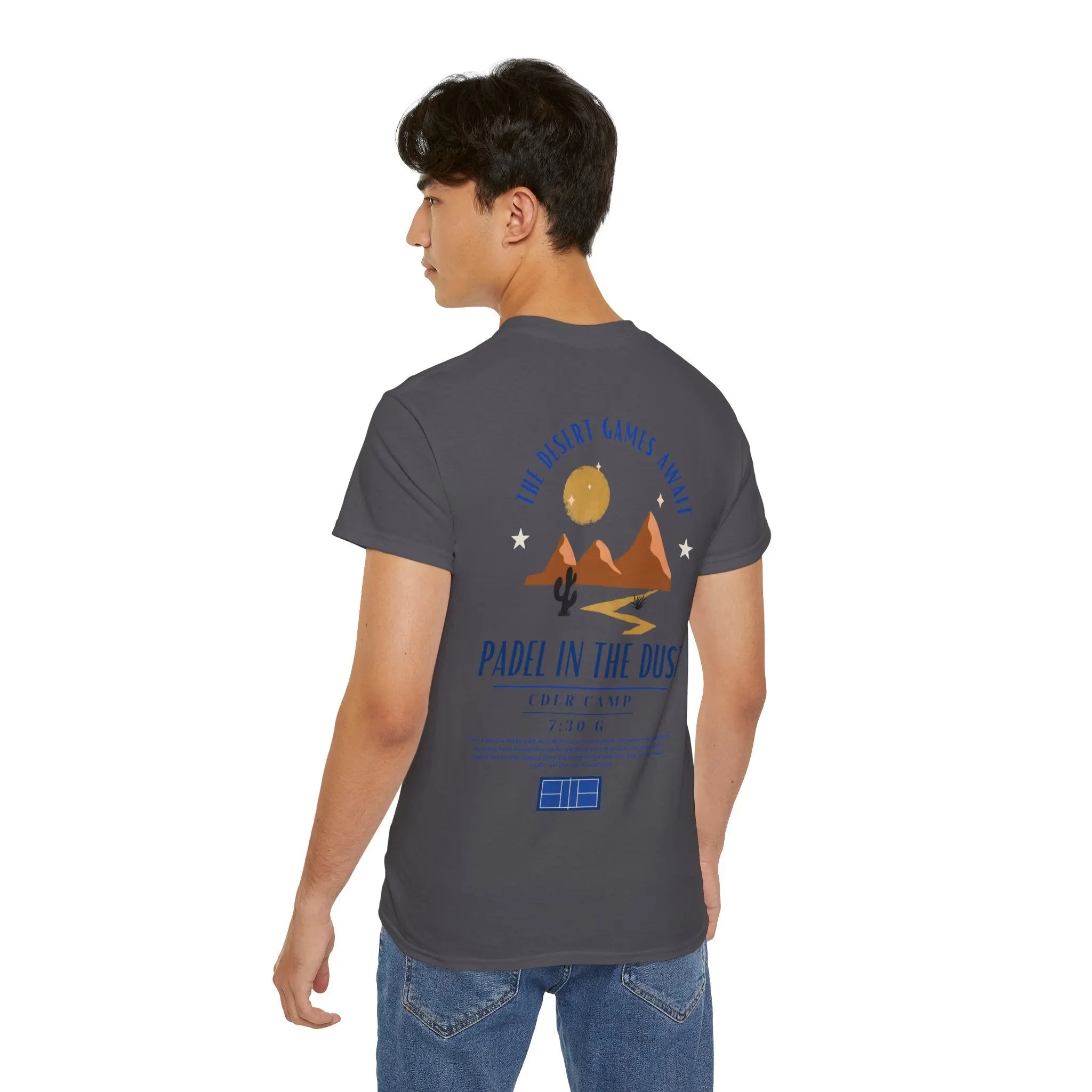 PSF Collective A young man wears the Printify Limited Edition - Padel in the Dust Tee: dark gray with a desert scene and "THE DESERT GAMES 19-24"—ideal for fans of the Burning Man padel shirt vibe. Designed for the Unwind