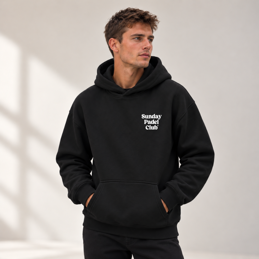 PSF Collective A man with short brown hair looks to the side, wearing a black Sunday Padel Club Hoodie with a front kangaroo pocket and the brand name in white, rounded lettering on the upper left chest, standing against a plain, light gray background with soft shadows. Designed for the Unwind