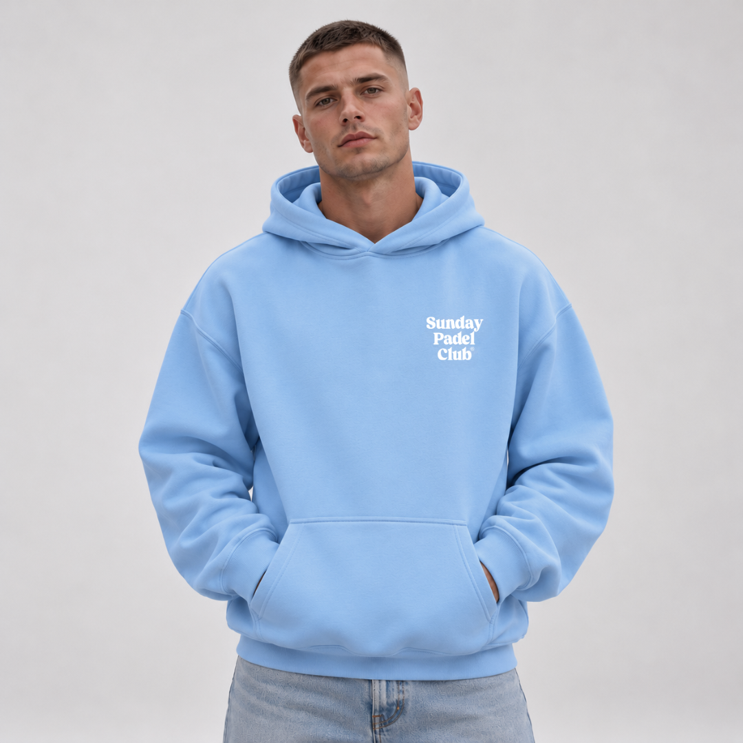PSF Collective A man with short brown hair wears a bright blue Sunday Padel Club Hoodie in Carolina Blue with a front pocket and white lettering, posed against a plain light grey background. Designed for the Unwind
