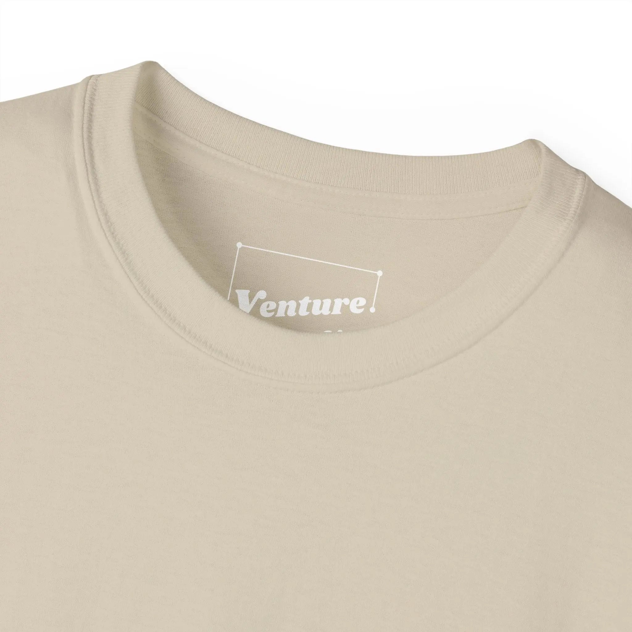 PSF Collective Close-up of the beige Limited Edition "Human Being" Tee by Printify, featuring the collar and part of the chest. The white label inside reads Venture. Shirt is laid flat on a white background. Designed for the Unwind