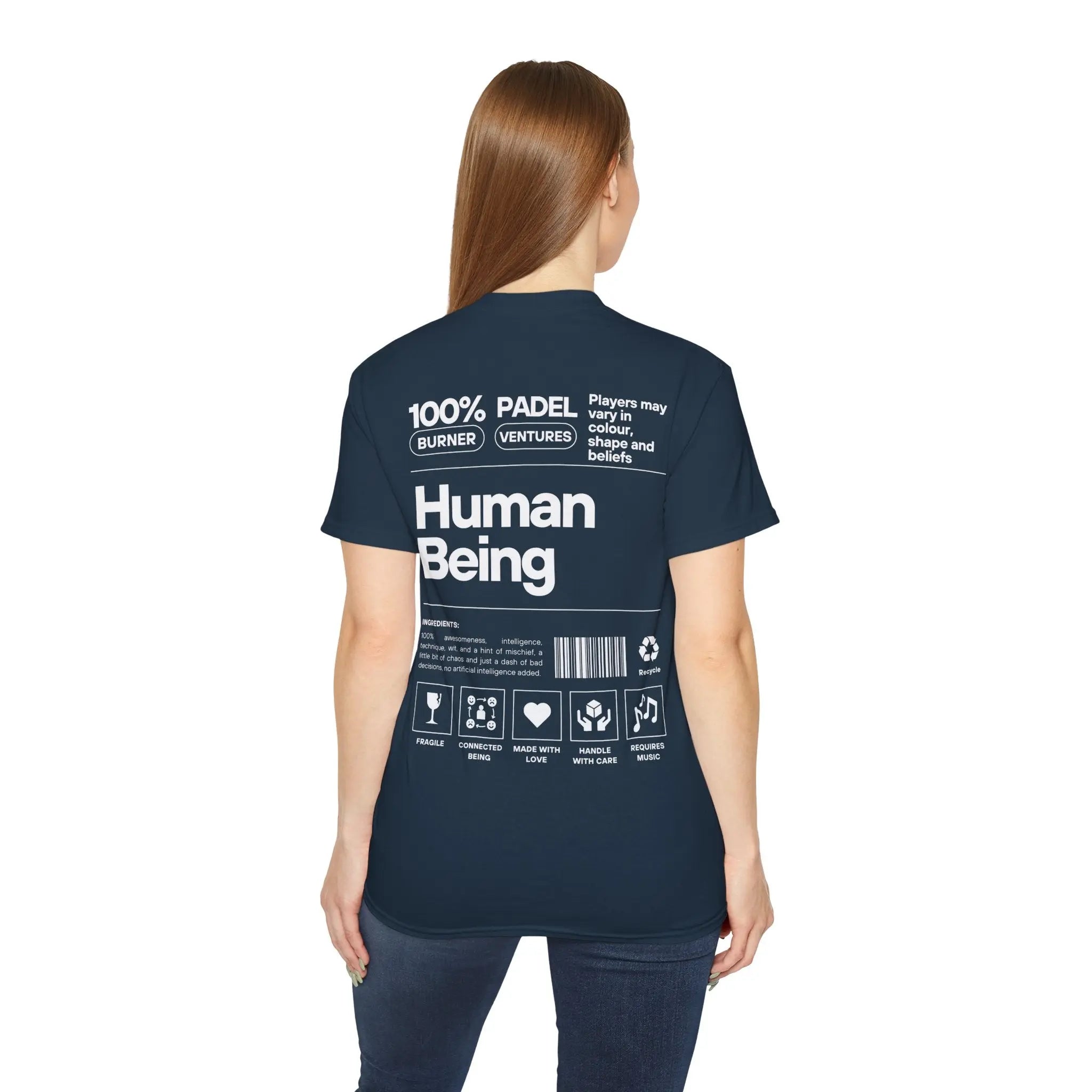 PSF Collective A woman with long brown hair, seen from behind, wears the Printify Limited Edition "Human Being" Tee in navy. The back features bold white text reading “100% Human Being” with icons and phrases styled like a product label. Designed for the Unwind