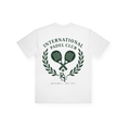 PSF Collective Introducing the International Crest Box Tee: a white T-shirt featuring "INTERNATIONAL PADEL CLUB" in green, positioned above two crossed padel rackets inside a laurel wreath. Beneath the design are the initials "ISF" and the text "MALLORCA • EST. 2024," all in green. This heritage tee showcases the signature crest on the back, offering post-match style that's perfect for padel enthusiasts. Designed for the Unwind