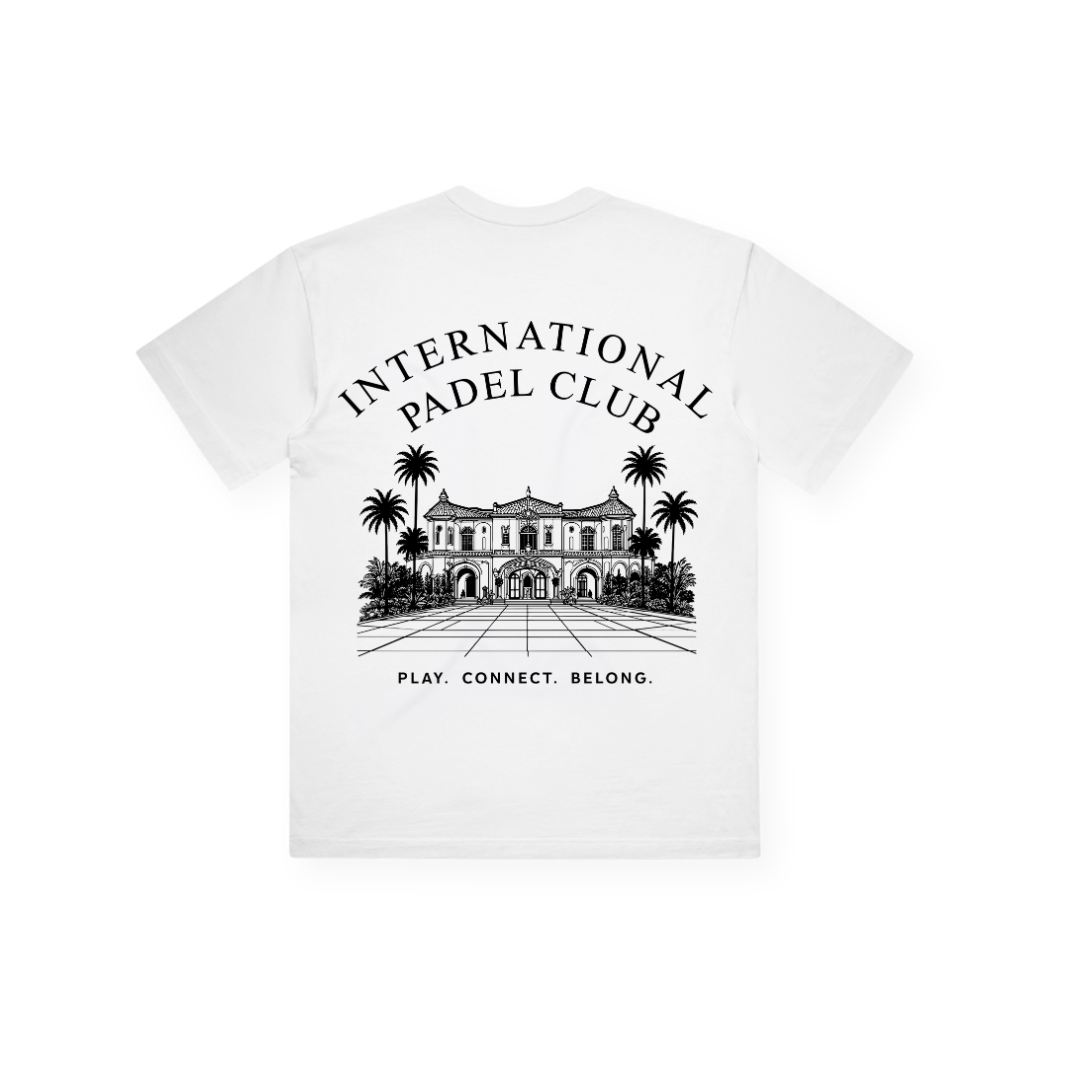 PSF Collective Introducing the Padel Club House Box Tee: crafted in white cotton, this tee showcases an intricate black illustration of a grand building with palm trees. The centered graphic on the upper back features "INTERNATIONAL PADEL CLUB" above and "PLAY. CONNECT. BELONG." below, combining style with sustainability in one statement piece. Designed for the Unwind