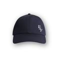 PSF Collective A plain navy Heritage Cap viewed from the front, featuring the white letters PSF embroidered on the right front panel. The background is white with a soft shadow around the cap. Designed for the Unwind