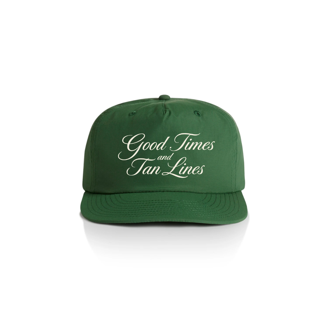 PSF Collective The Good Times and Tan Lines Cap is a green summer hat with white cursive text, a structured fit, and a flat brim. It’s photographed on a white background with even lighting. Designed for the Unwind